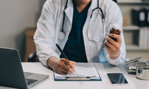 Handsome young doctor with a beard and a lab coat taking of his glasses to read an email in his laptop